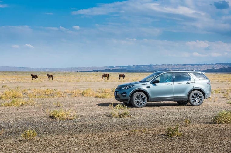Land Rover Discovery Sport parked in steppe with horses in the background